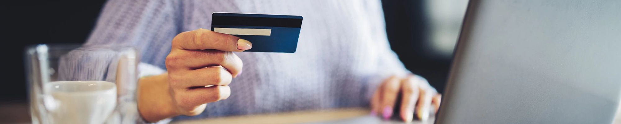woman holding credit card while working at laptop